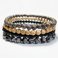 Stack of beaded bracelets of pyrite, tourmaline, snowflake obsidian, and jasper on a white surface.