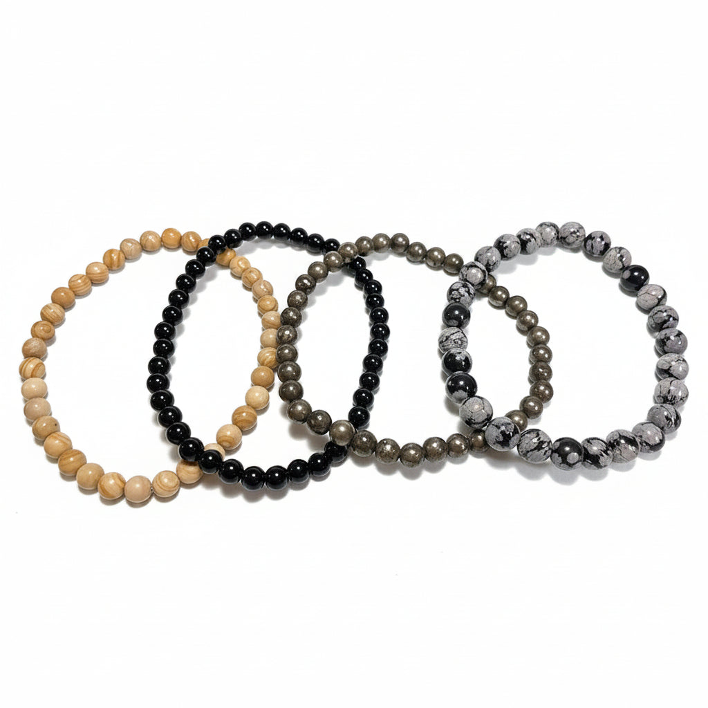Set of four bracelets of jasper, tourmaline, pyrite, and obsidian on a white surface.