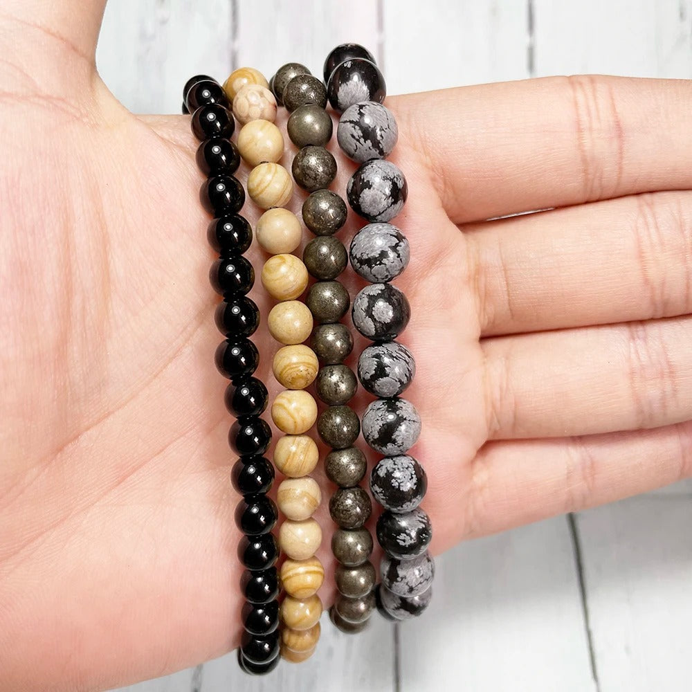 Set of four beaded bracelets of tourmaline, jasper, pyrite, and osidian on a hand against a light background.