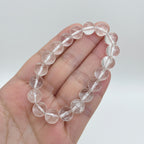 Clear quartz bracelet held in a hand with a white studi background