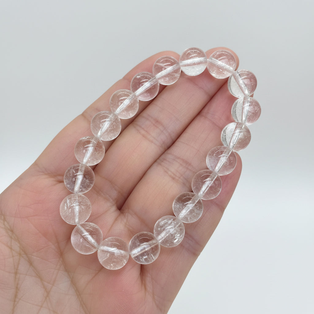 Clear quartz bracelet held in a hand with a white studi background