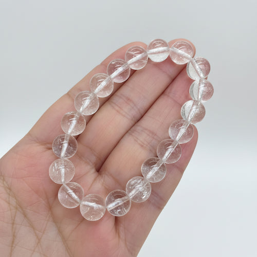 Clear quartz bracelet held in a hand with a white studi background
