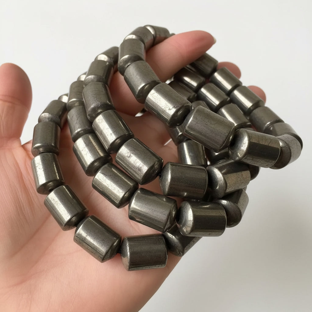 Hand holding four pyrite barrel beaded bracelets.
