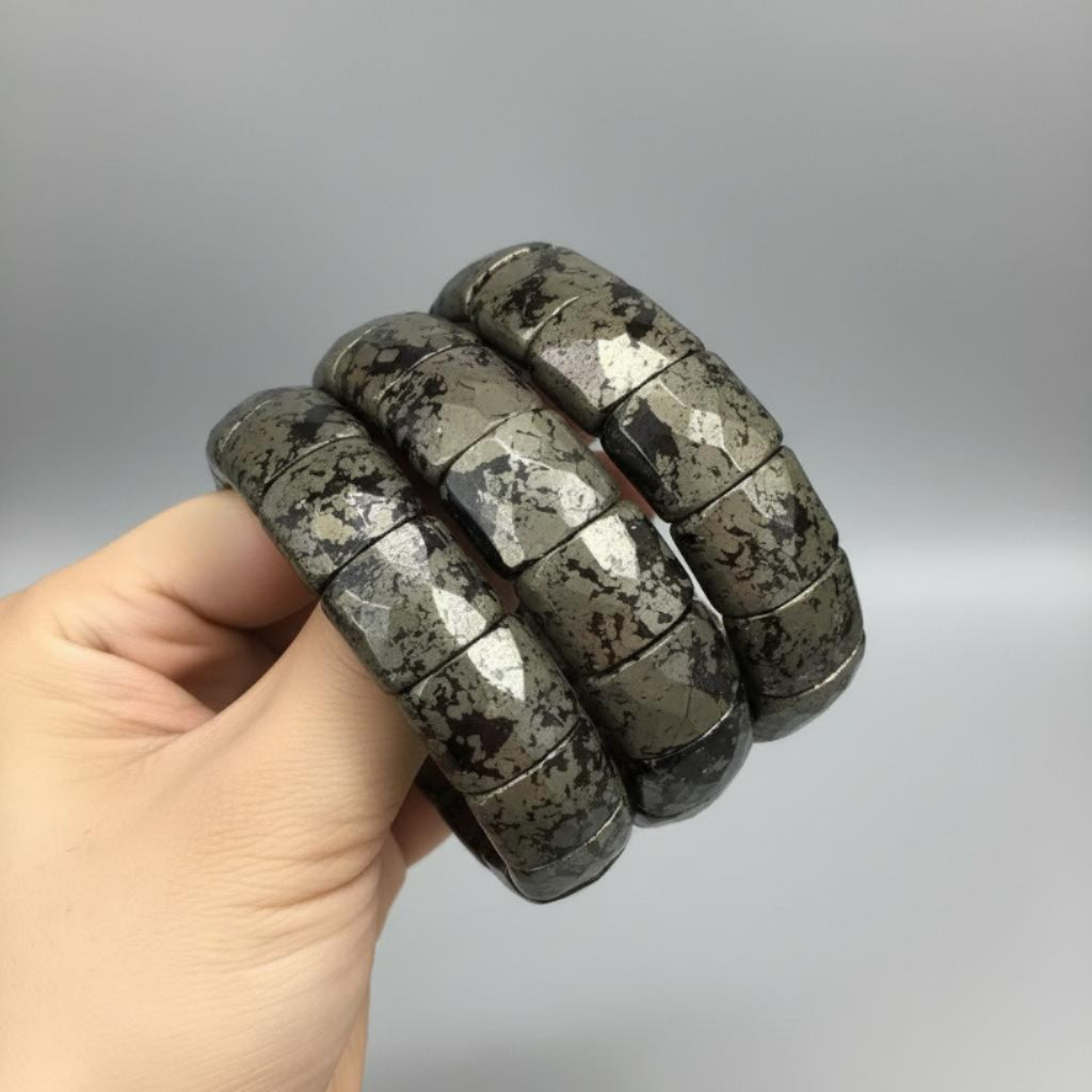 Hand holding a stack of textured, pyrite bracelets against a gradient background