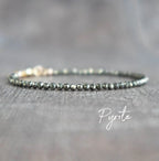 Pyrite beaded bracelet with gold clasp on a gray textured surface.