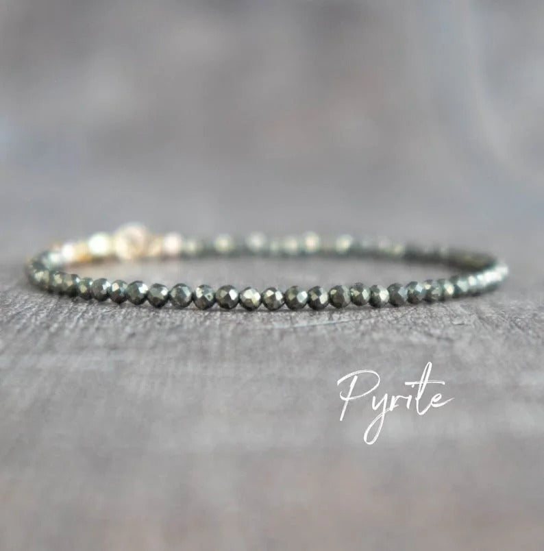 Pyrite beaded bracelet with gold clasp on a gray textured surface.