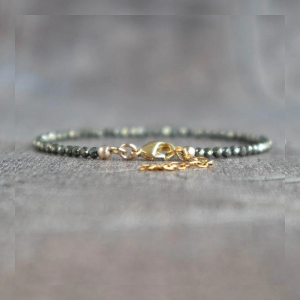 Pyrite beaded bracelet with gold clasp on a gray textured surface.